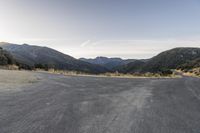 a motorcycle is going down an empty road by the mountains and trees at sunset time