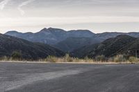 a motorcycle is going down an empty road by the mountains and trees at sunset time