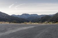 a motorcycle is going down an empty road by the mountains and trees at sunset time