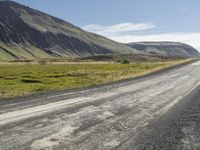 there is a motorcycle riding along a long gravel road in the mountains backlit by the sun