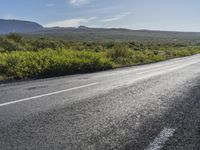 a black and white motorcycle is on the road by bushes and a field with mountains