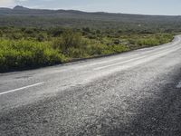 a black and white motorcycle is on the road by bushes and a field with mountains