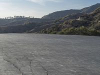 a motorcycle riding in the middle of a empty area with mountains in the distance nearby