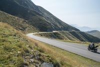 a motorcycle parked on a small mountain side road near mountains with no cars driving on it