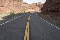 a person riding a motorcycle along a narrow road through rocks and sand cliffs a grassy area on both sides