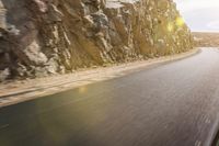 the back end of a motorcycle riding down a road in front of a steep mountain