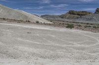 there is a man on a motorcycle riding in the field on dirt, and two mountains behind him