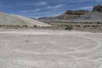 there is a man on a motorcycle riding in the field on dirt, and two mountains behind him