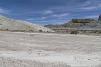 there is a man on a motorcycle riding in the field on dirt, and two mountains behind him