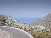 a person rides a red motorcycle down a winding road with mountains in the background under a blue sky