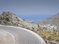 a person rides a red motorcycle down a winding road with mountains in the background under a blue sky