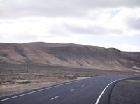 a person on a motorcycle going down the road through a desert area and mountains on either side