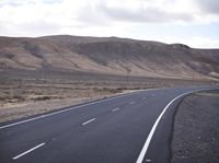 a person on a motorcycle going down the road through a desert area and mountains on either side