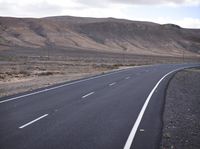 a person on a motorcycle going down the road through a desert area and mountains on either side