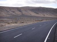 a person on a motorcycle going down the road through a desert area and mountains on either side