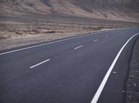 a person on a motorcycle going down the road through a desert area and mountains on either side