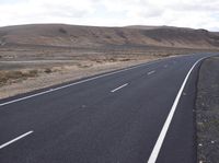 a person on a motorcycle going down the road through a desert area and mountains on either side