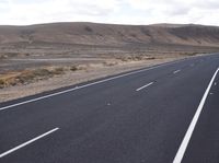 a person on a motorcycle going down the road through a desert area and mountains on either side