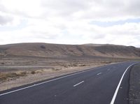 a person on a motorcycle going down the road through a desert area and mountains on either side