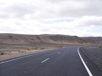 a person on a motorcycle going down the road through a desert area and mountains on either side