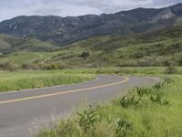 a motorcycle is parked on a rural road in the mountains near grass and trees with hills and bushes behind it