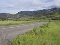 a motorcycle is parked on a rural road in the mountains near grass and trees with hills and bushes behind it