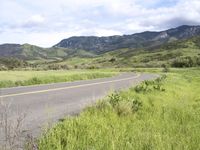 a motorcycle is parked on a rural road in the mountains near grass and trees with hills and bushes behind it