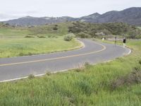 a motorcycle is parked on a rural road in the mountains near grass and trees with hills and bushes behind it