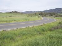 a motorcycle is parked on a rural road in the mountains near grass and trees with hills and bushes behind it