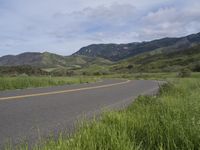 a motorcycle is parked on a rural road in the mountains near grass and trees with hills and bushes behind it