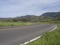 a motorcycle is parked on a rural road in the mountains near grass and trees with hills and bushes behind it