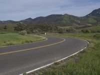 a motorcycle is parked on a rural road in the mountains near grass and trees with hills and bushes behind it