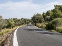 a motorcycle is traveling down a empty country road at an angle to a valley, surrounded by lush brush and trees