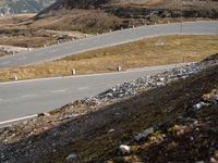 a motorcycle travels down the side of a mountain road in front of a fenced hill