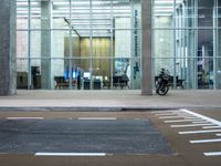 a motorcycle parked in front of a building with glass doors on it and an empty parking space