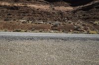 two motorcycles driving down the road near a mountain side area with sparse vegetation and rocks