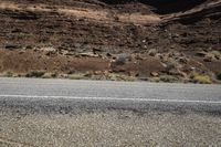 two motorcycles driving down the road near a mountain side area with sparse vegetation and rocks