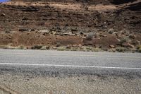 two motorcycles driving down the road near a mountain side area with sparse vegetation and rocks