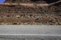 two motorcycles driving down the road near a mountain side area with sparse vegetation and rocks