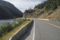 two motorcycles driving along the side of the road in front of some mountains and water