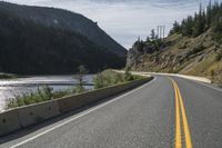 two motorcycles driving along the side of the road in front of some mountains and water