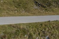 two motorcycles are parked on the side of a road in front of a hill, with grass and rocks scattered around the road