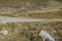 two motorcycles are parked on the side of a road in front of a hill, with grass and rocks scattered around the road