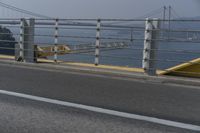 a motorcyclist on the road by the water and bridge, with the road to the left