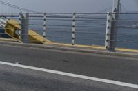 a motorcyclist on the road by the water and bridge, with the road to the left