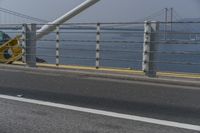 a motorcyclist on the road by the water and bridge, with the road to the left