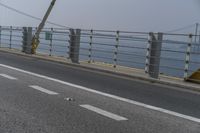 a motorcyclist on the road by the water and bridge, with the road to the left