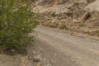 a person on a motorcycle on a gravel road with rocks and trees near them on the side