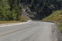 a man riding on a motorcycle down the middle of the road next to a mountain