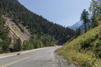 a man riding on a motorcycle down the middle of the road next to a mountain